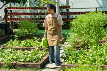 Asian female gardener walking in her backyard vegetable garden while holding a green watering can, demonstrating the essence of organic home gardening, sustainability, and healthy living.