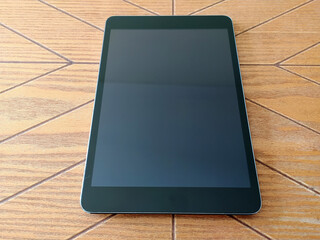 Sleek black tablet with blank screen rests on a wood surface. Perfect for technology, app, or website mockups. Clean and minimalist design. Ideal for showcasing your product or design. © SolaruS