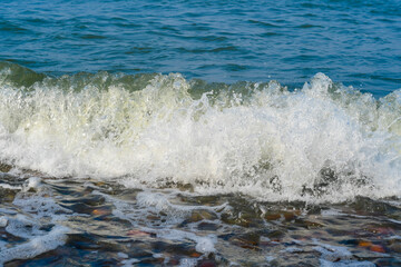 Close-up of waves crashing onto a rocky shore. Sea pebbles in the water.
