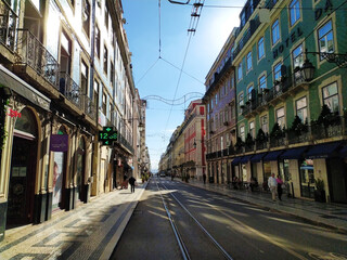 Fototapeta premium Sunny Lisbon street scene with colorful buildings, tram tracks, and pedestrians.
