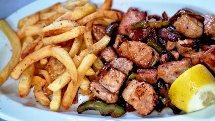 Plate with grilled meat, sautéed vegetables, crispy fries, and a slice of lemon