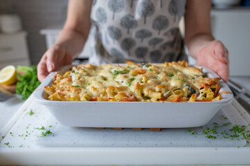 Woman with a fresh and homemade cooked vegetarian pasta, vegetable casserole in the kitchen