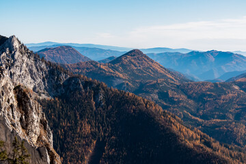 Scenic view of hilly landscape and mountains of Graz Highland and Glein Alps shrouded in mist seen from Pribitz, Hochschwab Alps, Styria, Austria. Rolling hills covered in forest vibrant autumn colors