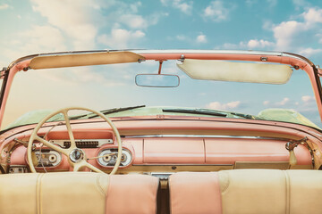 Driver view of a pink vintage classic open American cabriolet car in front of a sunny blue sky