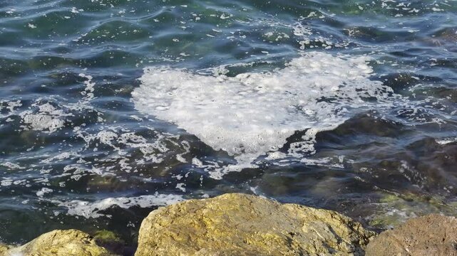 Handheld video shot of a large patch of dirt and pollution on the surface of the sea next to some rocks on the coast