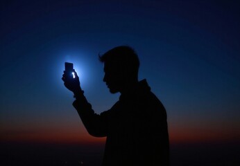 Silhouette of a Person Holding a Smartphone Against a Twilight Sky