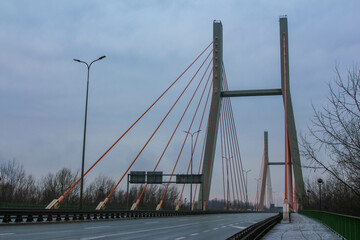 Modern cable-stayed bridge spans a quiet highway in overcast weather