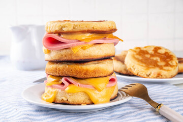 Breakfast crumpet sandwich, british pancake scones burger with cheese and ham, on kitchen table, with stack of crumpets and butter