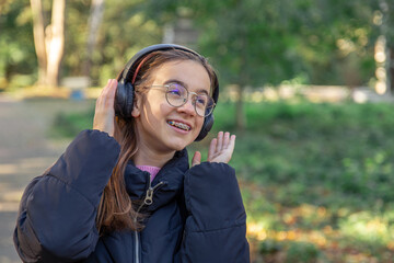 A happy girl is listening to music in headphones on a walk.