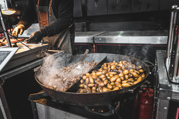 Fototapeta premium Chef grilling potatoes and vegetables over an open flame at a lively street food festival