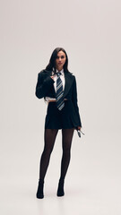 Casual yet stylish. Young woman wears black cropped blazer, white shirt, tie, short skirt and...