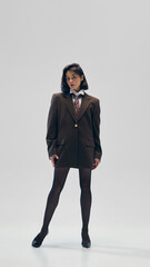 Full-length portrait of young beautiful woman wears black tights, brown oversized blazer with a...