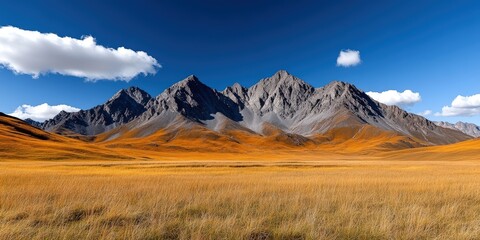 Fototapeta premium Majestic Mountain Range Under Bright Blue Sky with Fluffy Clouds and Golden Grassland Landscape
