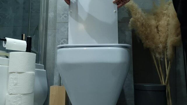 Man is opening modern toilet lid in bathroom