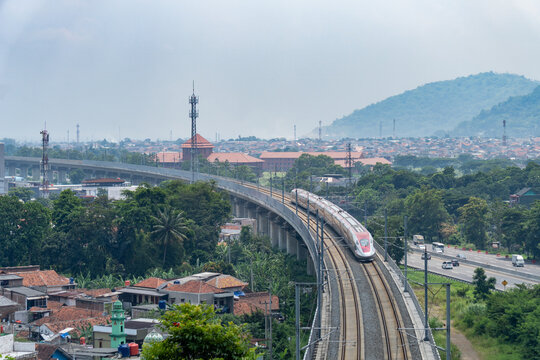 Jakarta Bandung High Speed Train railway turning on a bridge beside Purbaleunyi highway toll road, with Cimahi city skyline as background