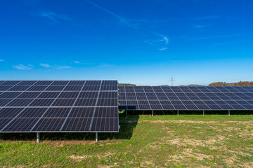 Photovoltaikanlage auf gr&uuml;ner Wiese mit Stromtrasse im Hintergrund