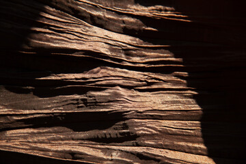 Close-up of textured fabric with deep shadows and highlights, showcasing its rich, brown color and...