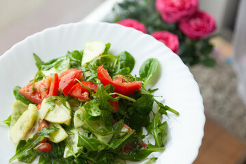 Fresh salad with tomatoes, cucumbers, and arugula on a white plate.