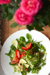 Fresh salad with tomatoes, cucumbers, and arugula, served on a white plate. A vibrant and healthy meal option.