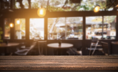 Empty wooden table in a sunlit cafe with blurred background of chairs and windows.