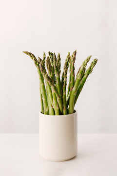 Several green asparagus in a large beige cup.