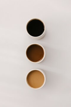 Three cups of coffee seen from above varying from black coffee to a splash of milk to latte colored coffee.