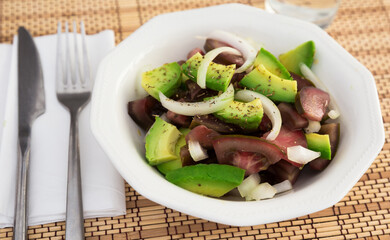 Salad of black tomatoes, avocado and onions in white ceramic bowl