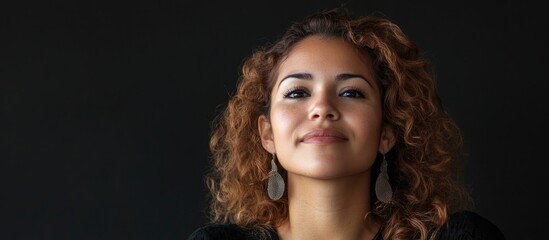 Fototapeta premium Smiling Hispanic woman with curly hair against a dark background creating ample negative space for text and design elements in a portraitual composition.