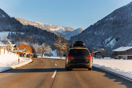Scenic back view family van car roof box rack luggage drive alpine countryside road cold winter day Europe mountain resort. Automobile vehicle holidays trip journey. Vacation transport seasonal scene