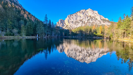Lake Kreuzteich surrounded by mountain peak Pribitz in Hochschwab Alps in Tragoess, Styria, Austria. Forest in vibrant autumn foliage. Crystal-clear water reflects majestic ridges. Mirror-like effect