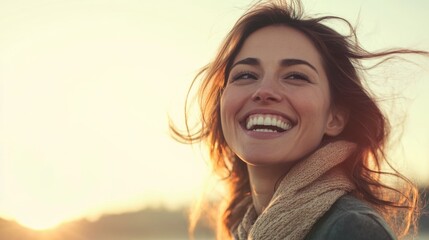 Fototapeta premium Cheerful smiling businesswoman with flowing hair against a bright sunset background featuring warm golden and soft pastel tones with ample copyspace.