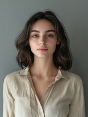 Obraz premium Brunette woman with natural makeup and wavy hair posing against a soft gray background, featuring ample copyspace for text and branding.