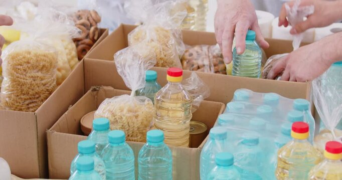Group of volunteers preparing free food donations of foodstuffs in cardboard boxes for poor people. Charity workers working together in charitable foundation. Humanitarian aid concept. 4k video.