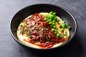 Mashed potatoes with beef meat and green peas in bowl. Dark background. Close up.