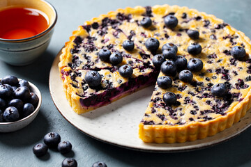 Blueberry tart with vanilla cream and cup of tea. Grey background. Close up.