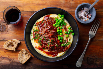 Mashed potatoes with beef meat, green peas in bowl and grass of red wine. Wooden background. Close up. Top view.