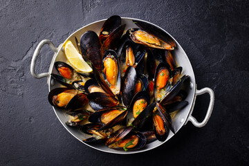 Mussels with herbs and sauce in black pan. Dark background. Close up. Top view.