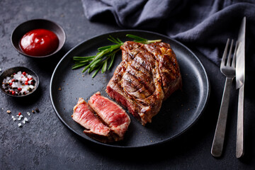 Beef Steak medium rare on a black plate. Dark grey background. Close up.