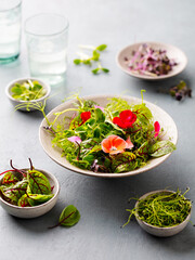 Green salad leaves with edible flowers in bowl. Grey background.