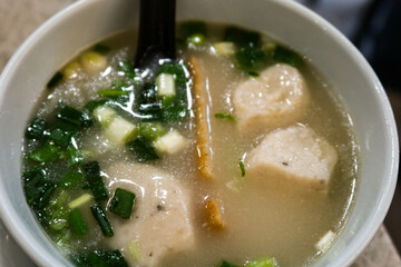 close up of Chinese Cantonese Hong Kong style soup with spring onion, white fish ball, fish slice and a black spoon