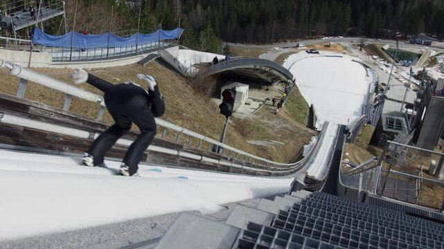 Ski jumper running down the ski jump, jumping and landing on the landing slope, high angle shot. Hills winter tournament concept.