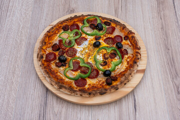 Paris, France - 11 06 2023: Italian culinary Still Life. A Mediterranean pizza with chorizo, ham, olives, green pepper and cheese seen from above and placed on a wooden tray.