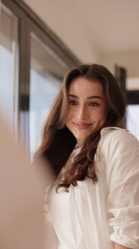 A smiling young woman looking at her reflection in a mirror, preparing and adjusting her appearance thoughtfully before attending a meeting.
