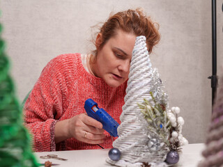 A woman is focused on crafting decorative holiday trees with glue and various embellishments. She...