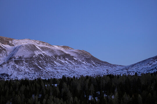 Montagne &eacute;rod&eacute;e et presque sans neige au printemps sous un ciel de fin du jour plongeant la vall&eacute;e bois&eacute;e dans la nuit.