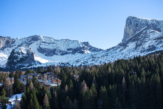 Vall&eacute;e enneig&eacute;e entre au pied d'une montagne avec village de station de ski nich&eacute; au milieu d'une for&ecirc;t de sapins.