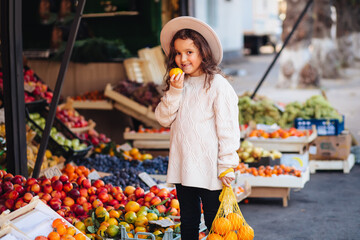 Cute little girl buying fruits and vegetables at organic farmers market.