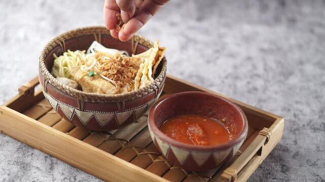 Women's Hands Sprinkle Fried Onions on Bakso Malang (Malang Meatballs) Served with Spicy Chili Sauce in a Rustic and Charming Arrangement, Highlighting the Art of Cultural Culinary and Delicious Cuisi