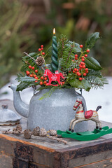 Weihnachts-Arrangement mit einer Kerze, Stechpalmenzweigen und Koniferenzweigen im alten Teekessel