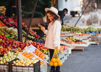 Cute little girl buying fruits and vegetables at organic farmers market.